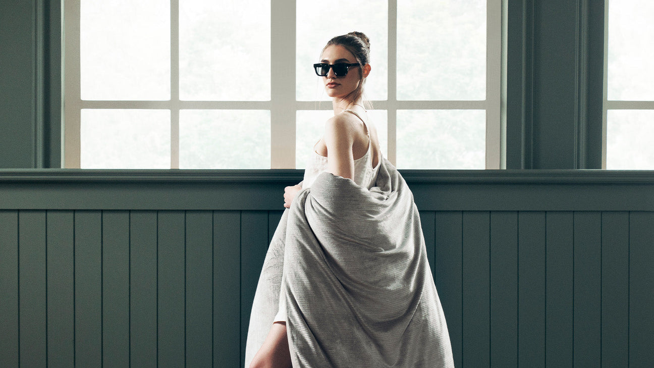 Woman wrapped in a soft textured quilt, showcasing the comfort, drape and artistry of thoughtfully crafted premium bedding.