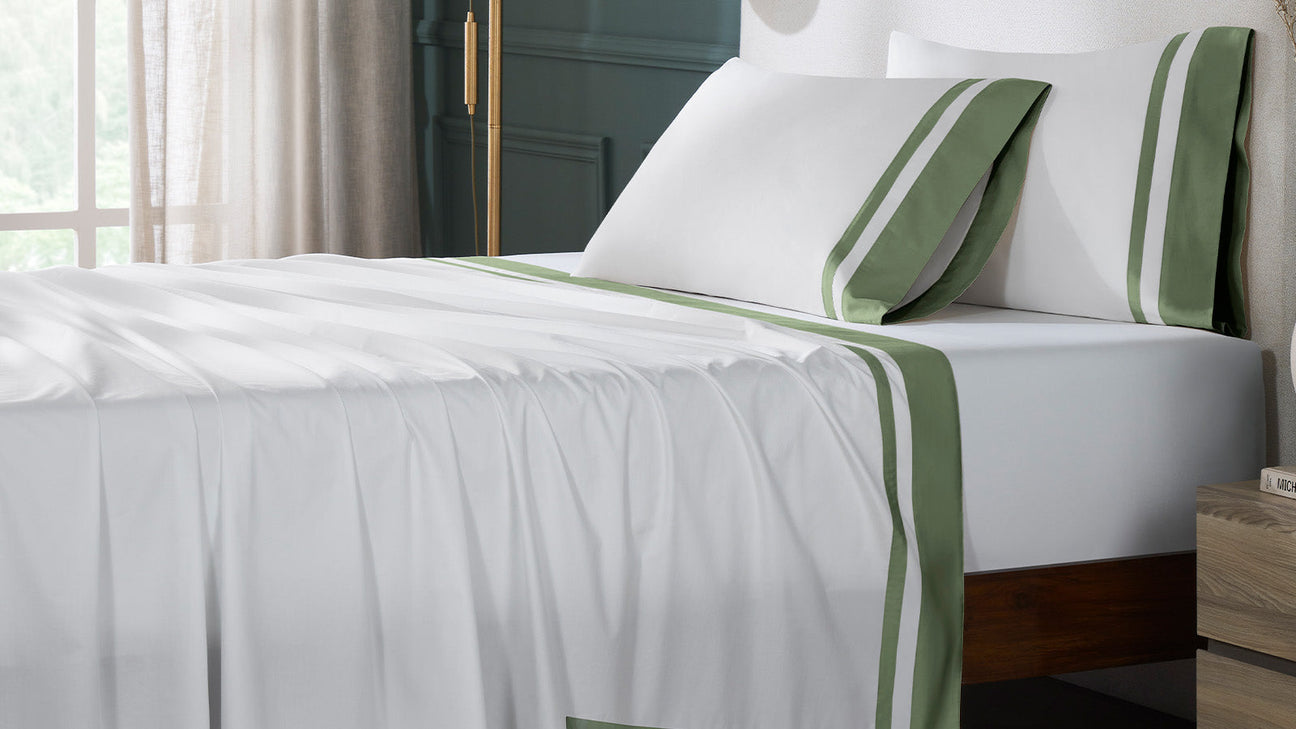 White bedding with green border detailing showcasing smooth premium sheets designed for elevated sleep comfort.