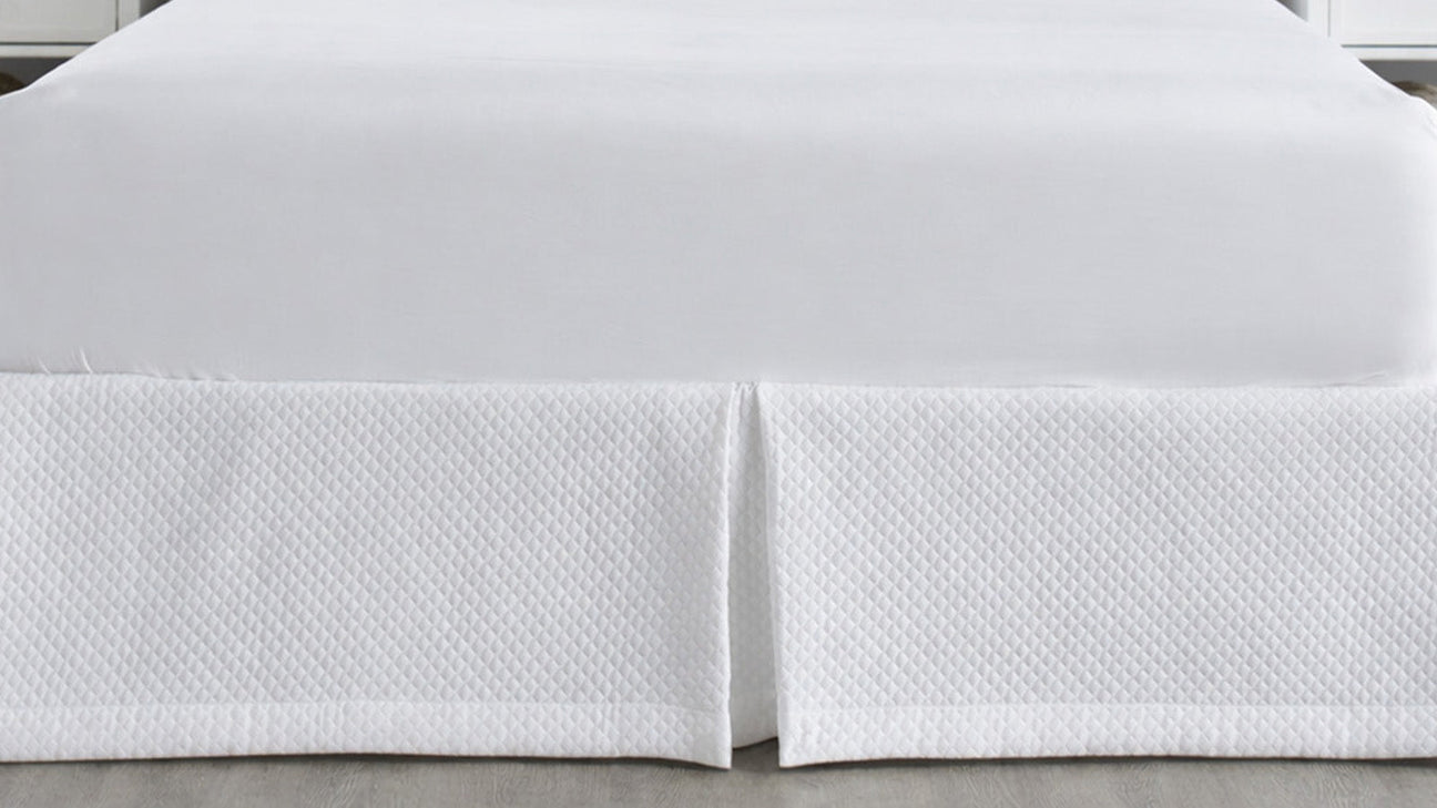 White quilted bed skirt with a tailored center pleat adding a clean, elegant finish to a luxury bed.
