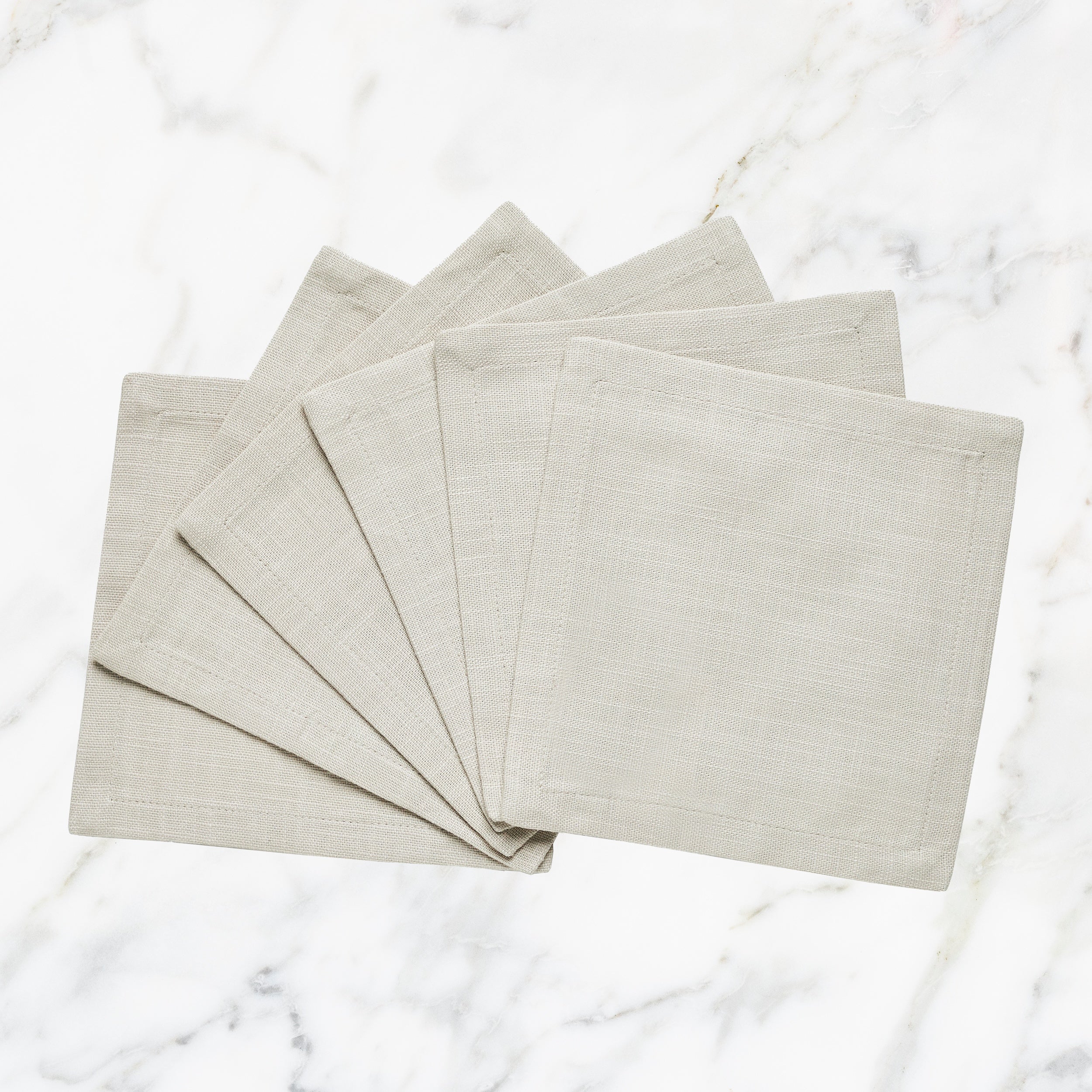 CNP-4912-66_1|Set of fan-folded natural beige linen dinner napkins on marble, ideal for elegant and reusable neutral table settings.