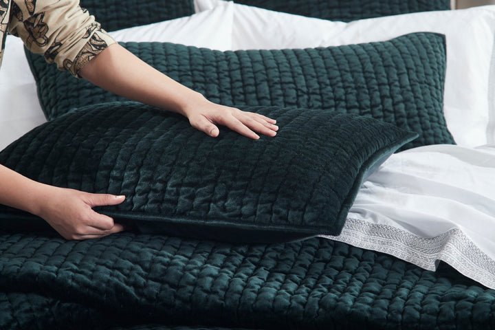 QT-363-9496_5|Hands adjusting a dark green velvet quilted throw pillow, showcasing its plush texture and rich color for elegant decor.