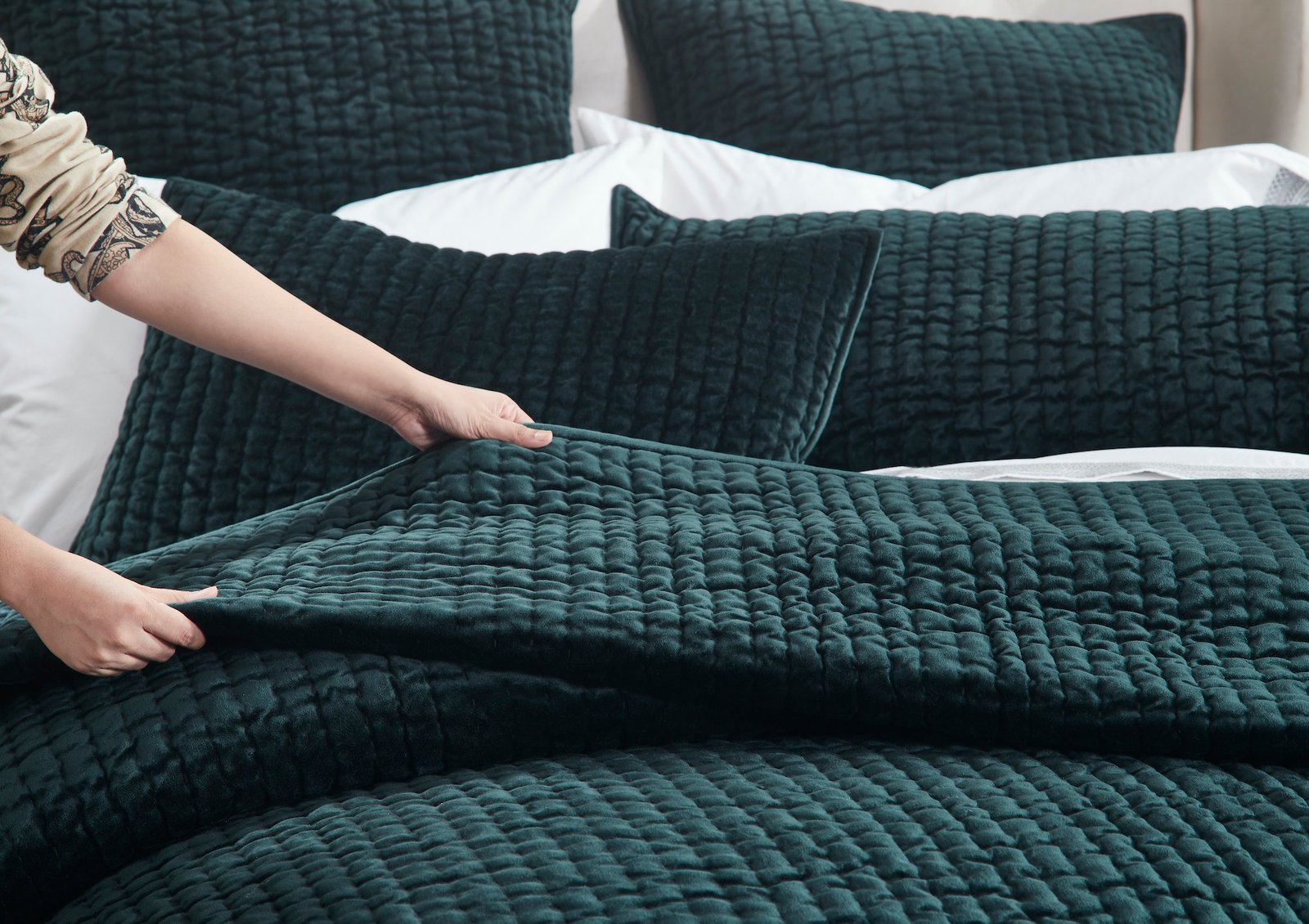 QT-363-11096_4|Hand gently adjusting the rich forest green quilted bed, highlighting the soft texture of the cozy and elegant quilt.