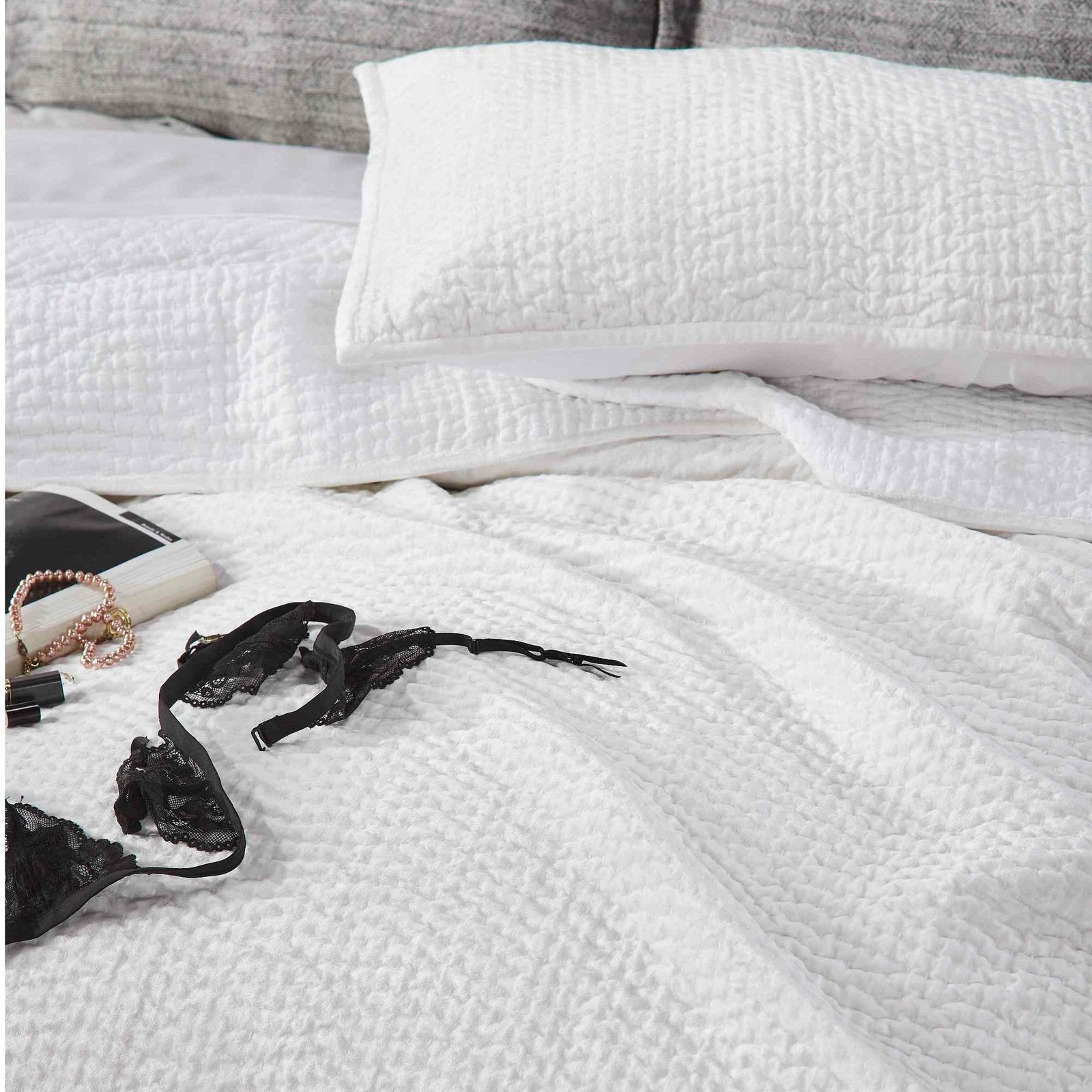 CL-182-9496_5|White textured coverlet on a bed with a black lace bra, soft quilted bedding for a cozy inviting private space. (118 chars)