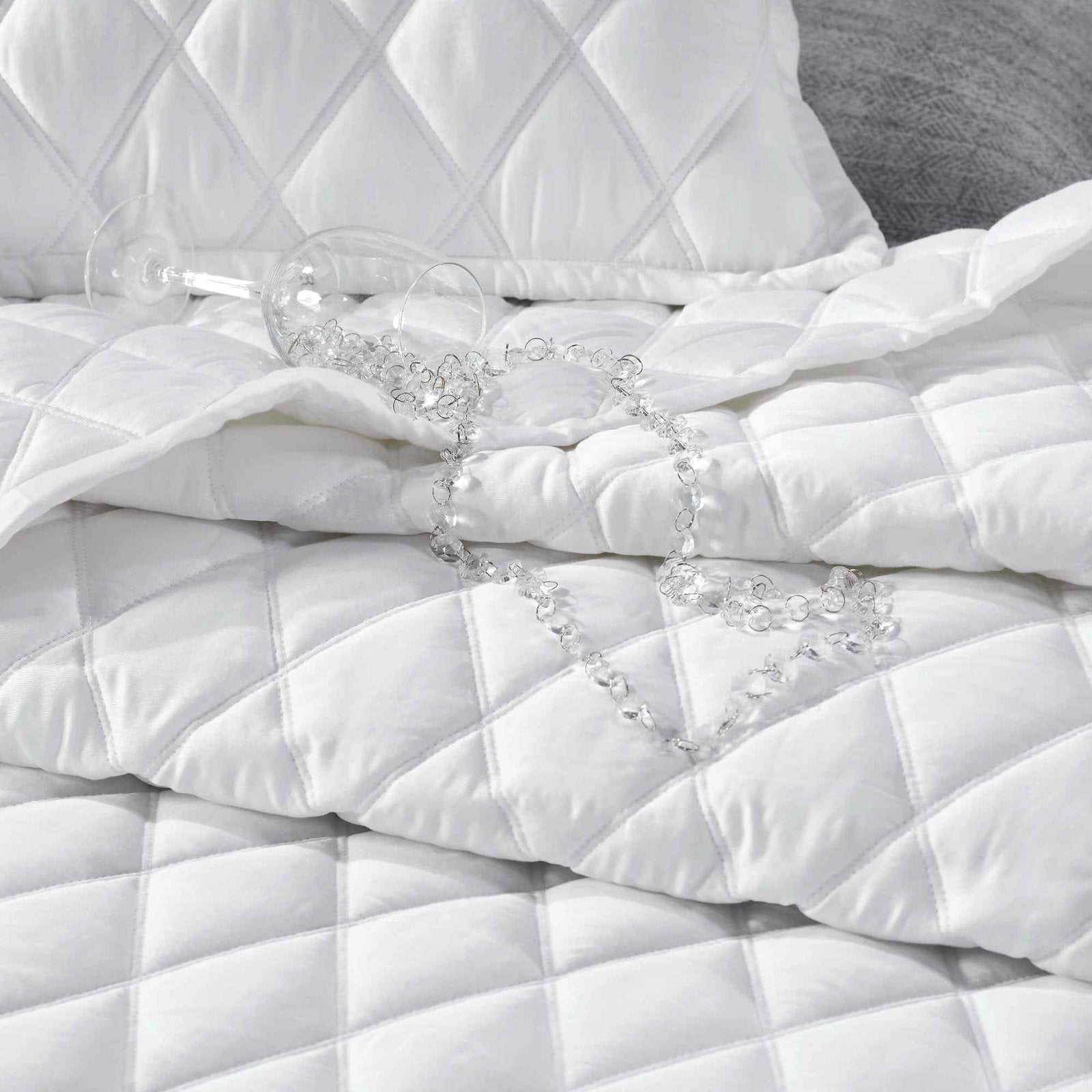CL-179-9496_4|White diamond-quilted coverlet with elegant sheen, perfect for luxury bedding. Accentuated by a sparkling necklace.