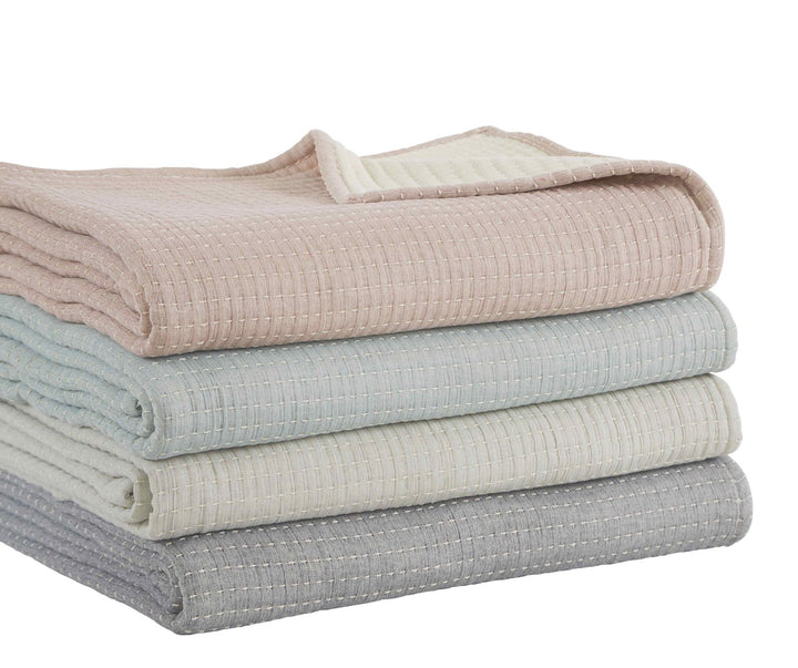 BT-106-9496_3|Stack of four folded textured reversible quilt blankets: soft pink, tranquil blue, creamy white, and neutral grey for varied bedding.
