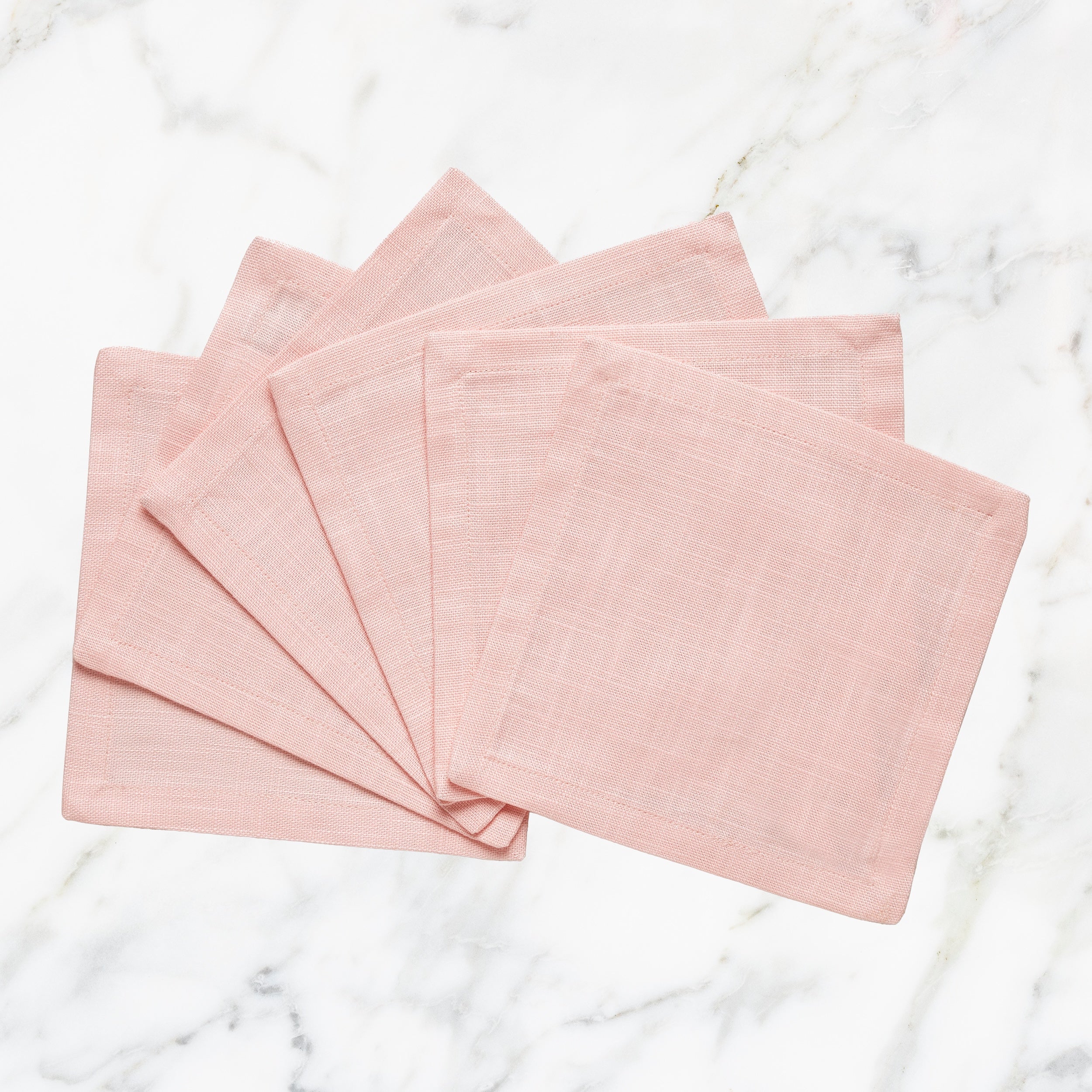 CNP-4910-66_1|Elegant fan of blush pink linen napkins arranged on a classic white marble surface, ideal for sophisticated table settings.