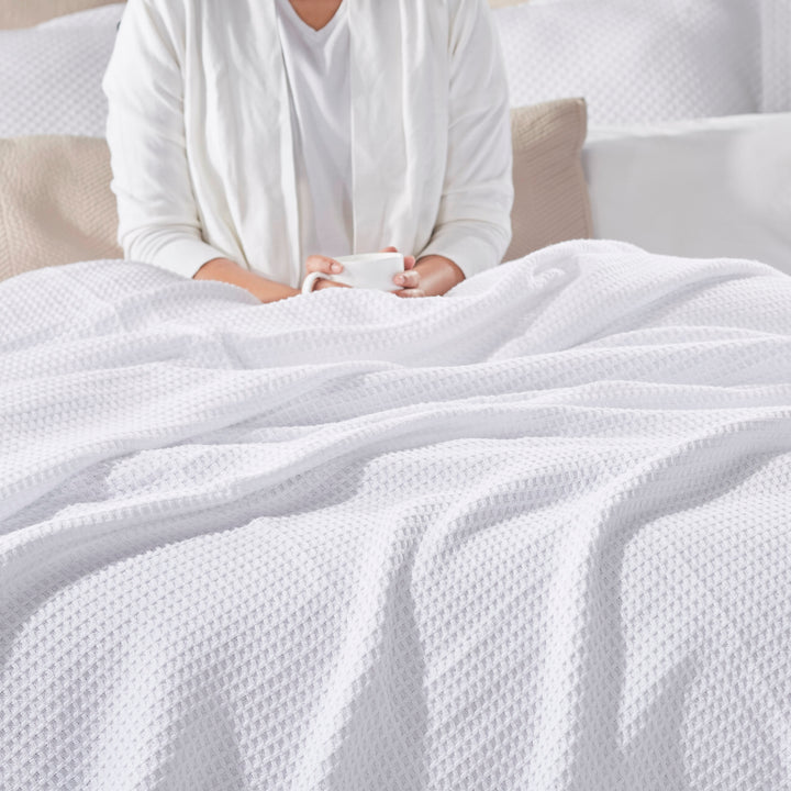 BL-855-9496_2|Plush white waffle weave blanket providing comfort for a person relaxing in bed, holding a mug for a cozy morning.