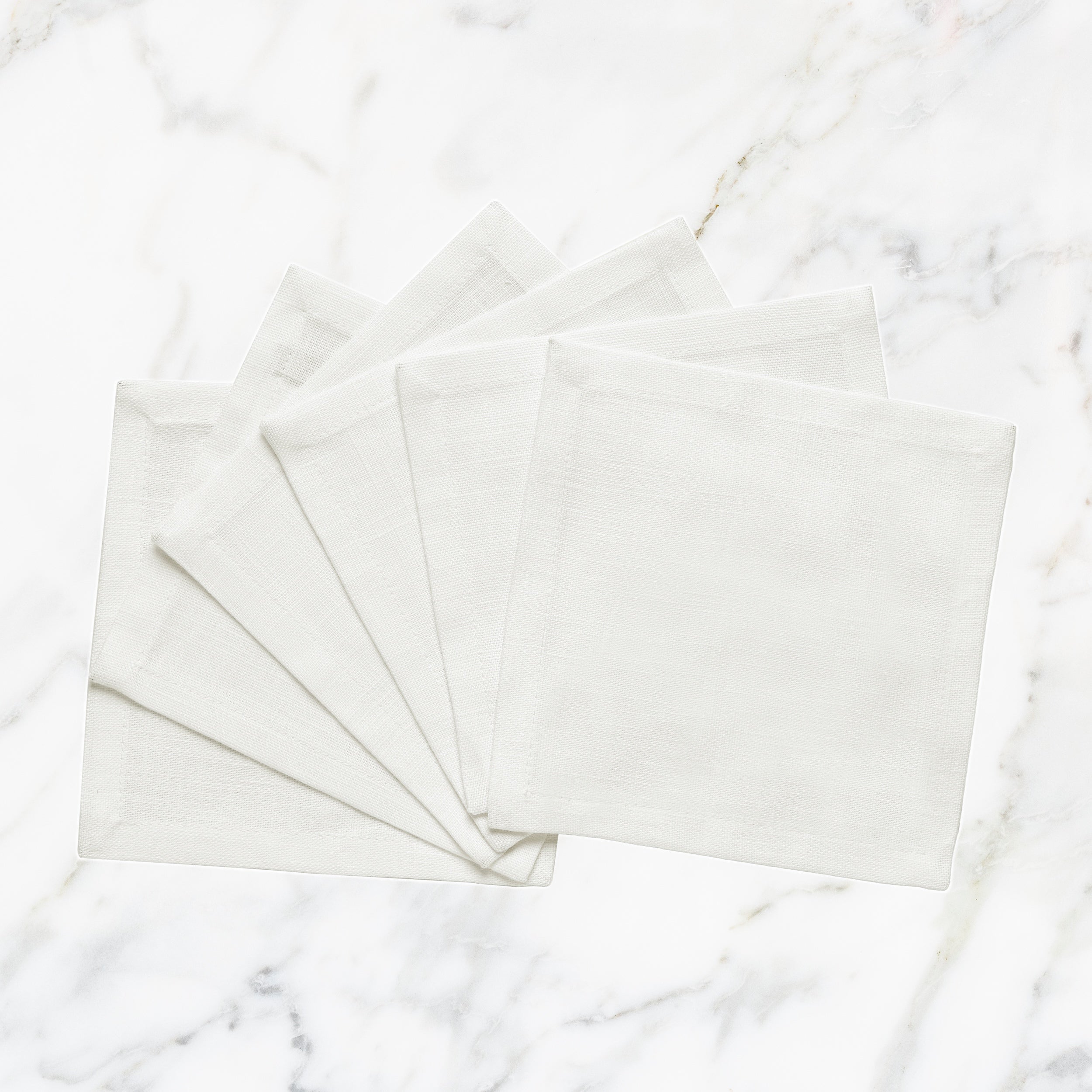 CNP-4908-66_1|Set of fanned white linen napkins displayed on a pristine white marble background for elegant table settings.