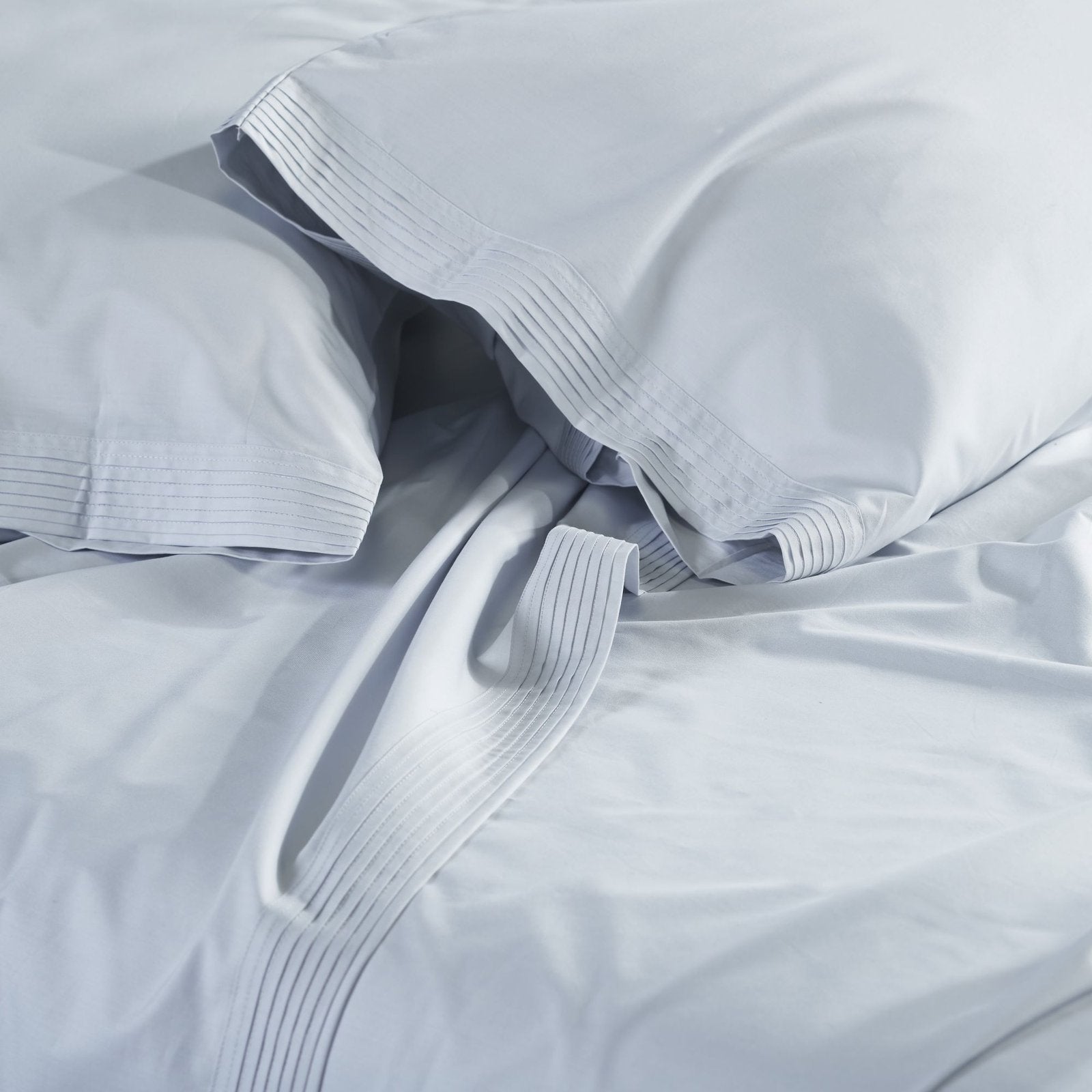 KSS-524-7880_3|Close-up of soft, smooth light blue 100% cotton sateen sheets and pillowcases, highlighting elegant pintuck hem details.