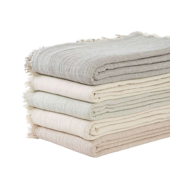 BT-115-9496_5|Stacked collection of soft, textured throw blankets in a palette of muted tones with stylish fringed edges.