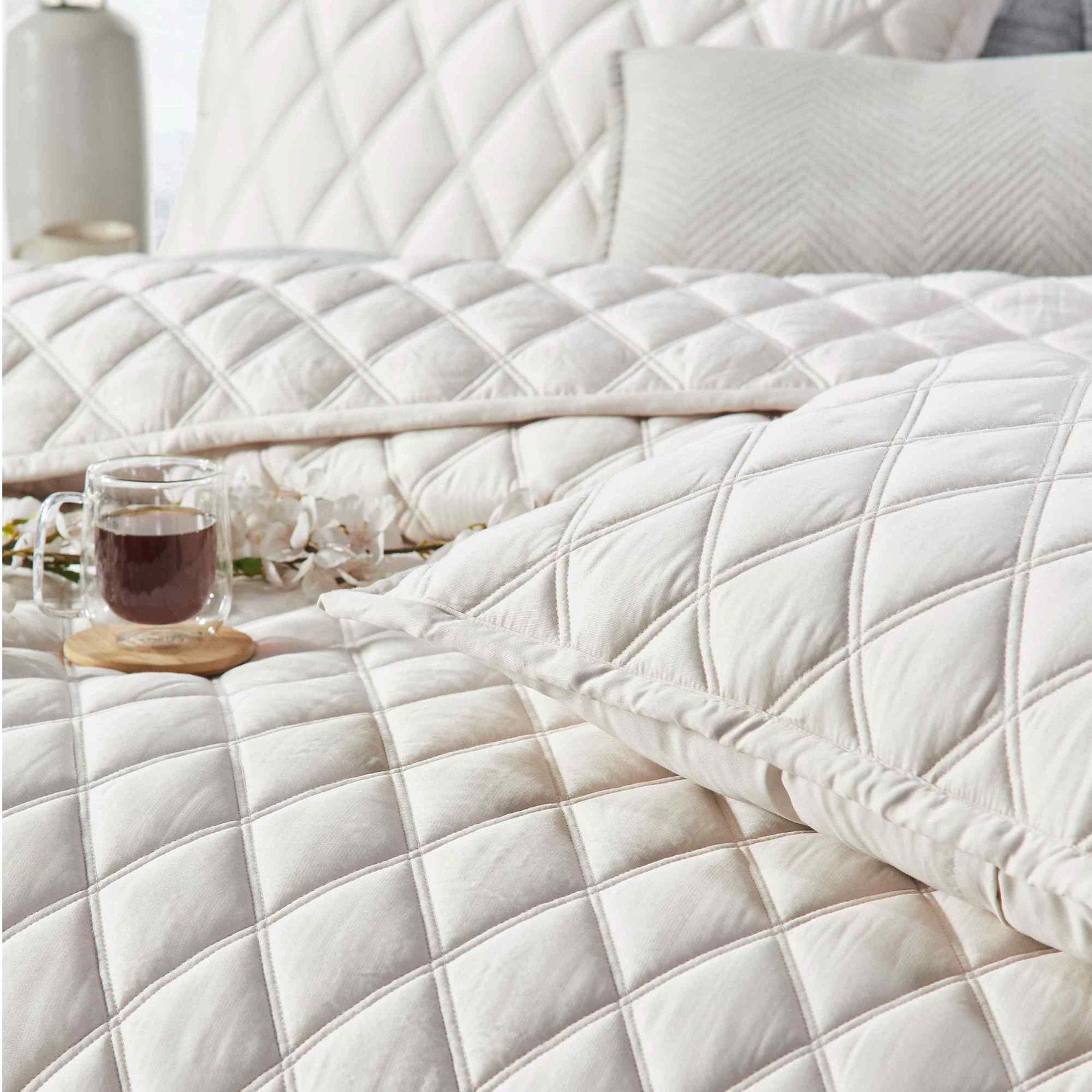 CL-180-9496_4|Cream diamond-quilted coverlet with elegant sheen, perfect for luxury bedding. Accentuated by a warm cup of tea.