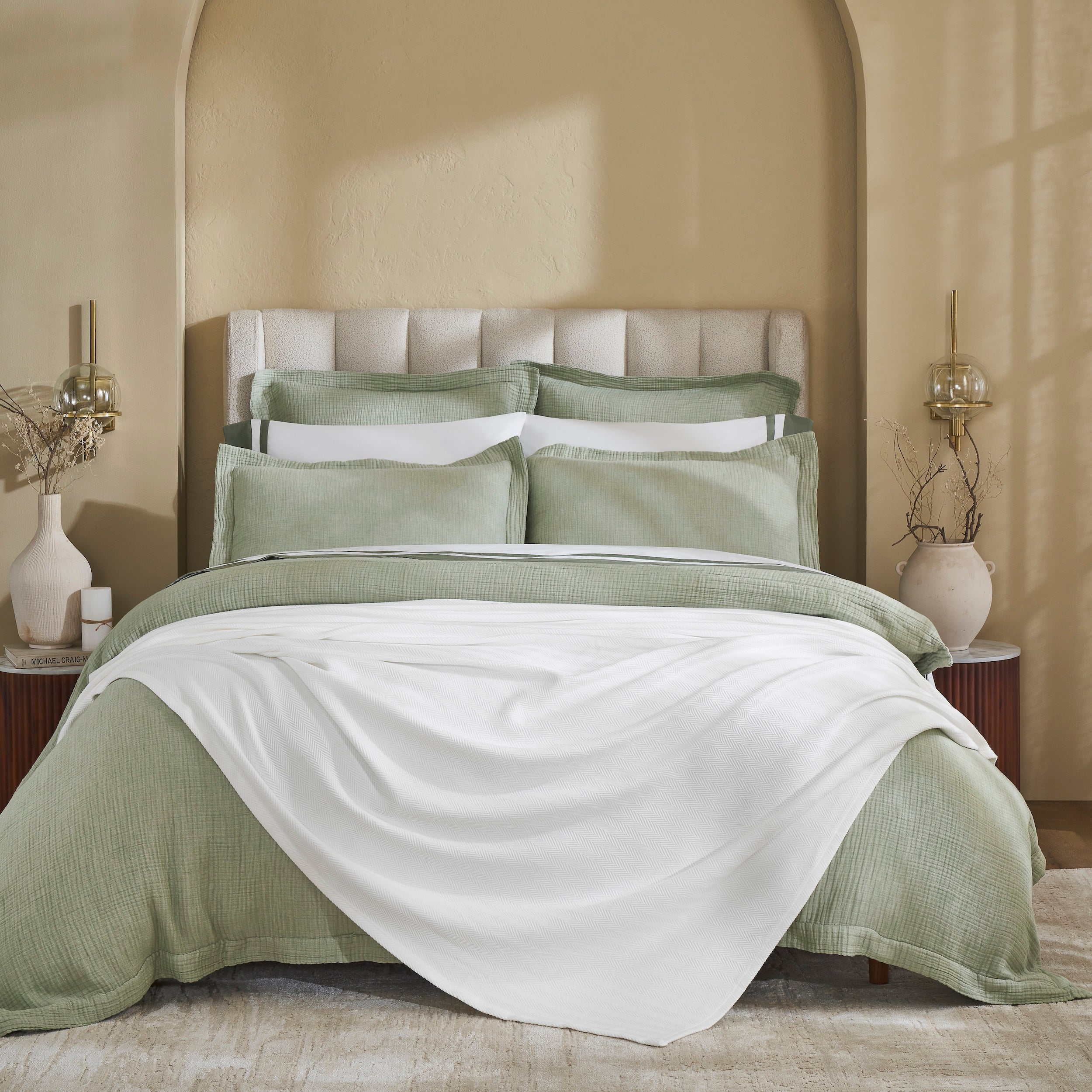 BL-865-9496_1|Soft white woven blanket draped over a sage green duvet, perfect for layering, adding warmth & elegant style to a modern bedroom.