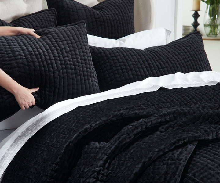 QT-361-9496_5|Hand holding up a plush black quilted pillow, showcasing the rich texture of the matching quilt and clean white sheets.