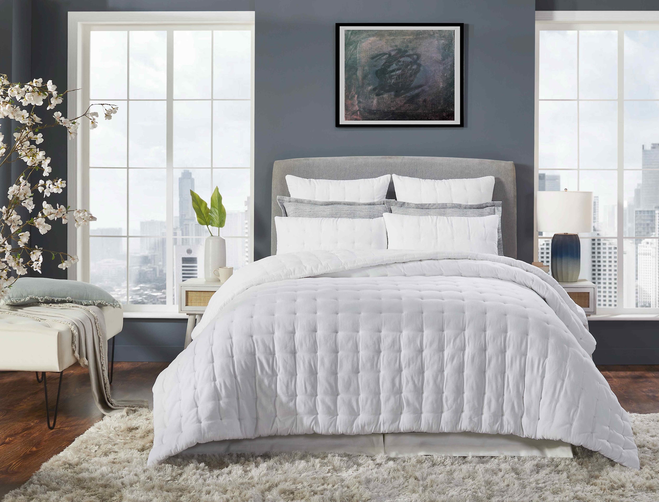 QT-353-9496_1|Modern white quilted bedding set on a king-size bed in a stylish bedroom with large windows overlooking a city skyline.