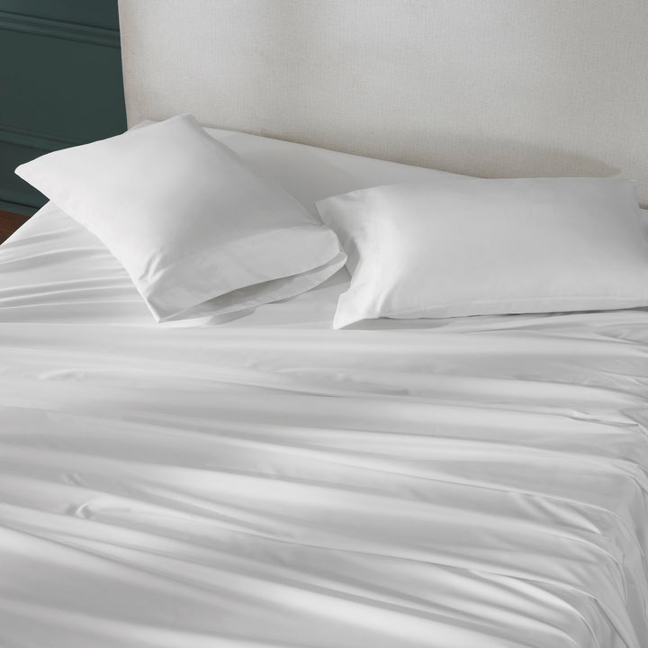 QSS-539-6080_3|Draped white 100% cotton sheets and two plump pillowcases on a bed, emphasizing the smooth, crisp fabric.
