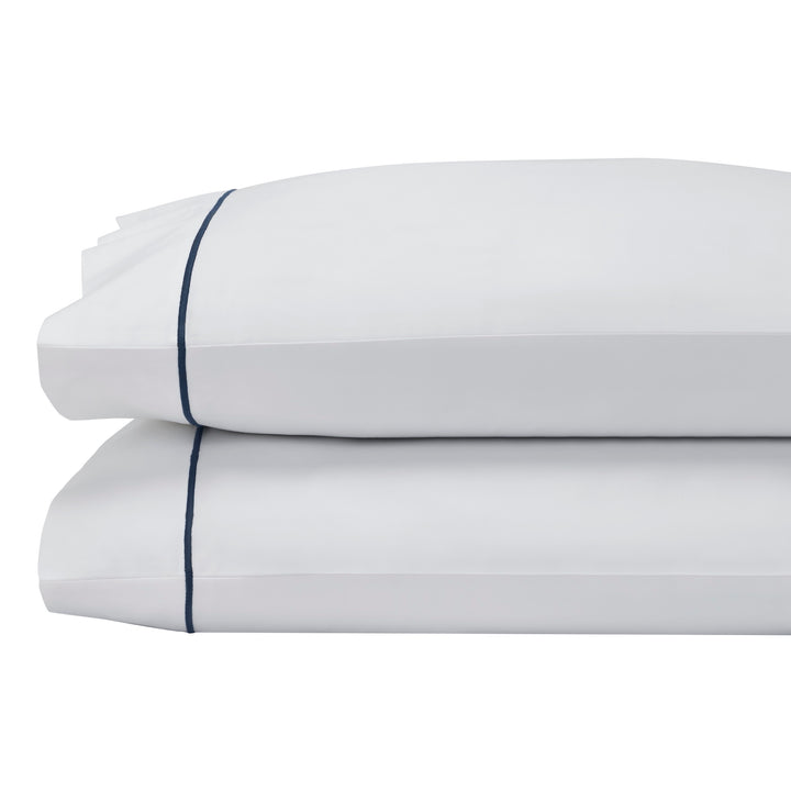 AKP-549-2040_2|Stacked luxurious 100% cotton pillowcases, featuring soft white fabric with subtle navy blue piped edges, for elegant bed comfort.