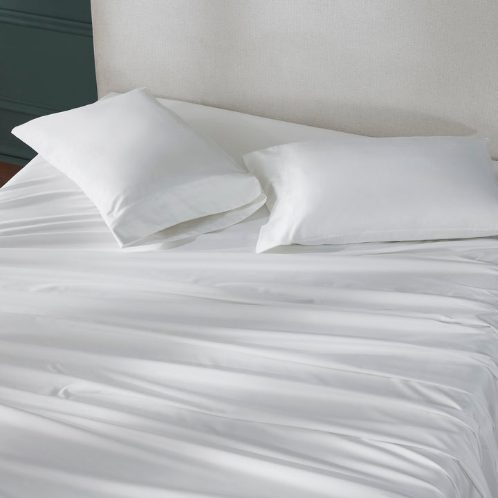 QSS-535-6080_3|Draped white 100% cotton sheets and two plump pillowcases on a bed, emphasizing the smooth, crisp fabric.
