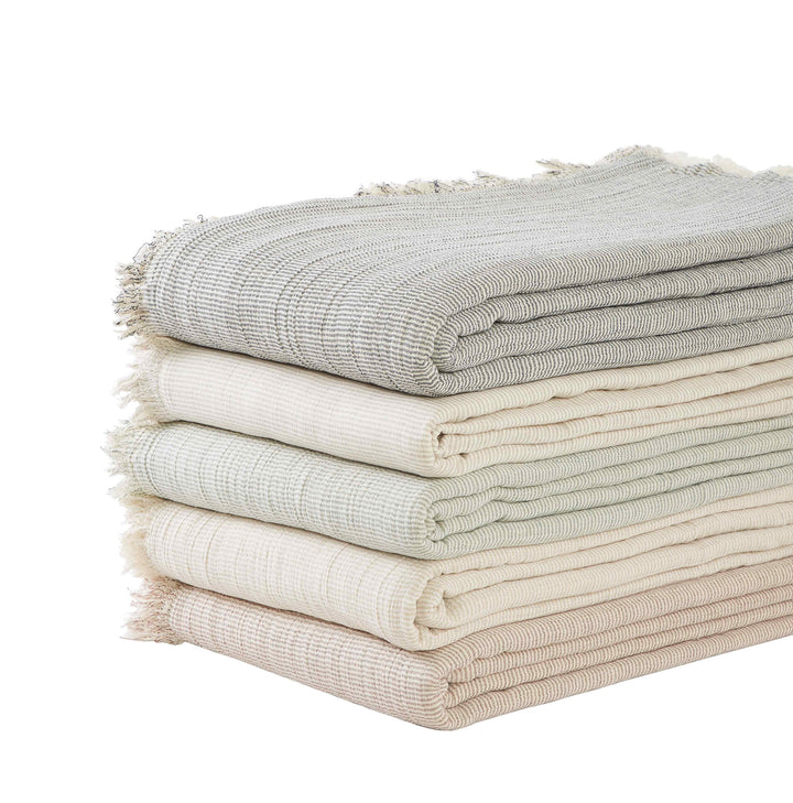 BT-111-X_2|Stack of assorted neutral striped cotton blankets with elegant fringe edges, offering comfort and style for home decor.