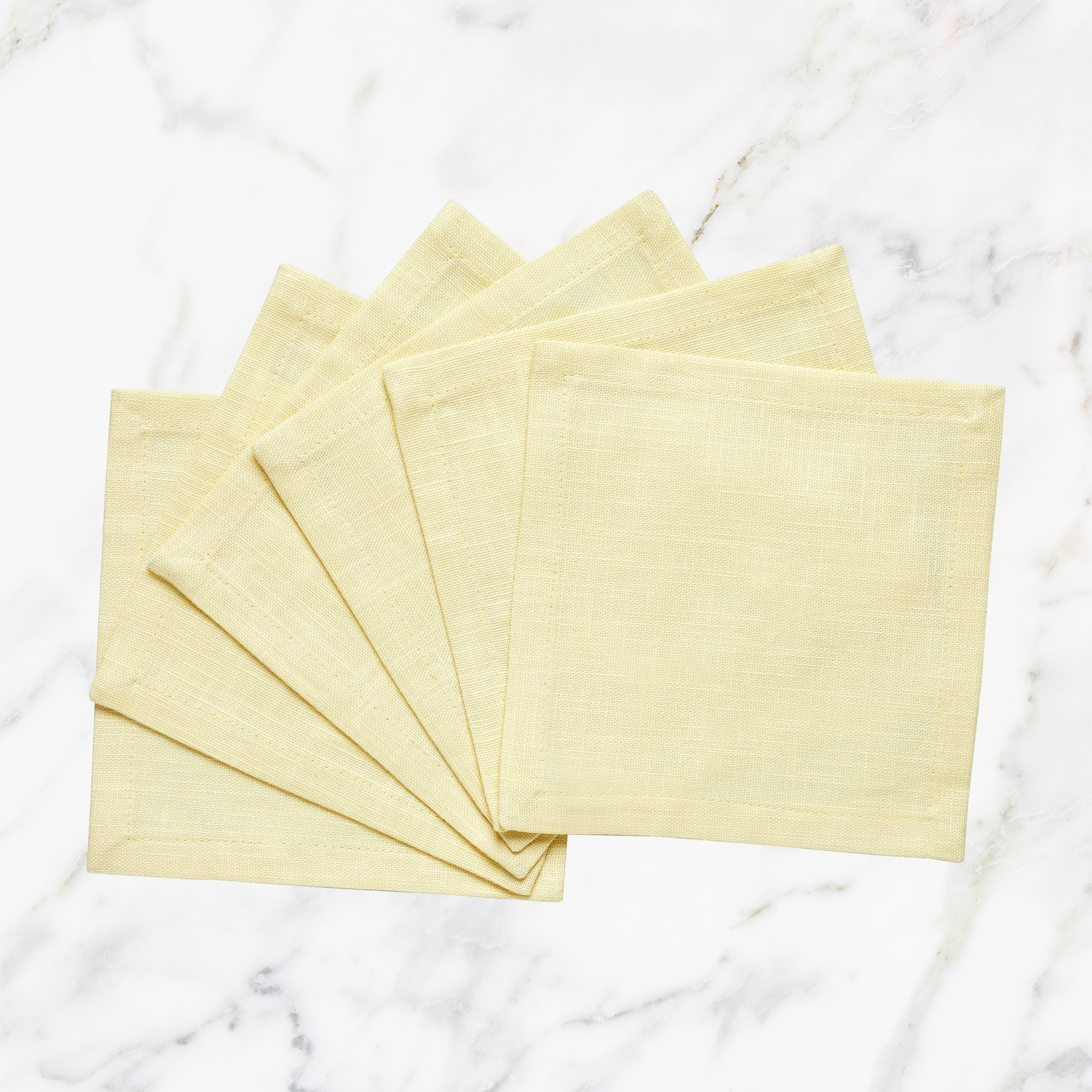 CNP-4907-66_1|Elegant set of light yellow linen fabric dinner napkins, fanned on a luxurious white marble background, perfect for entertaining.