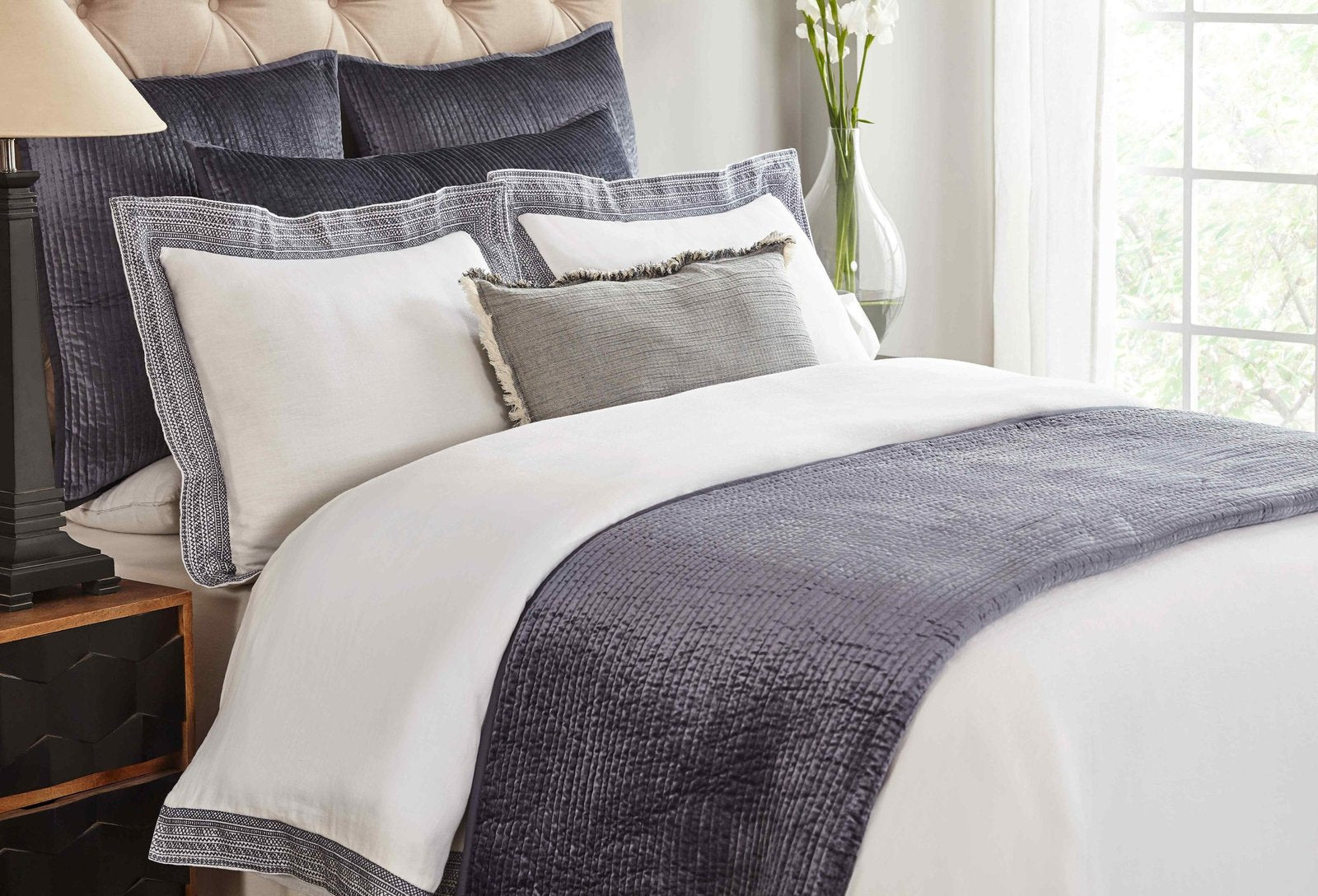 CL-159-11898_3|Dark blue quilted coverlet with a textured, ribbed pattern at the foot of a bed in a bright bedroom.