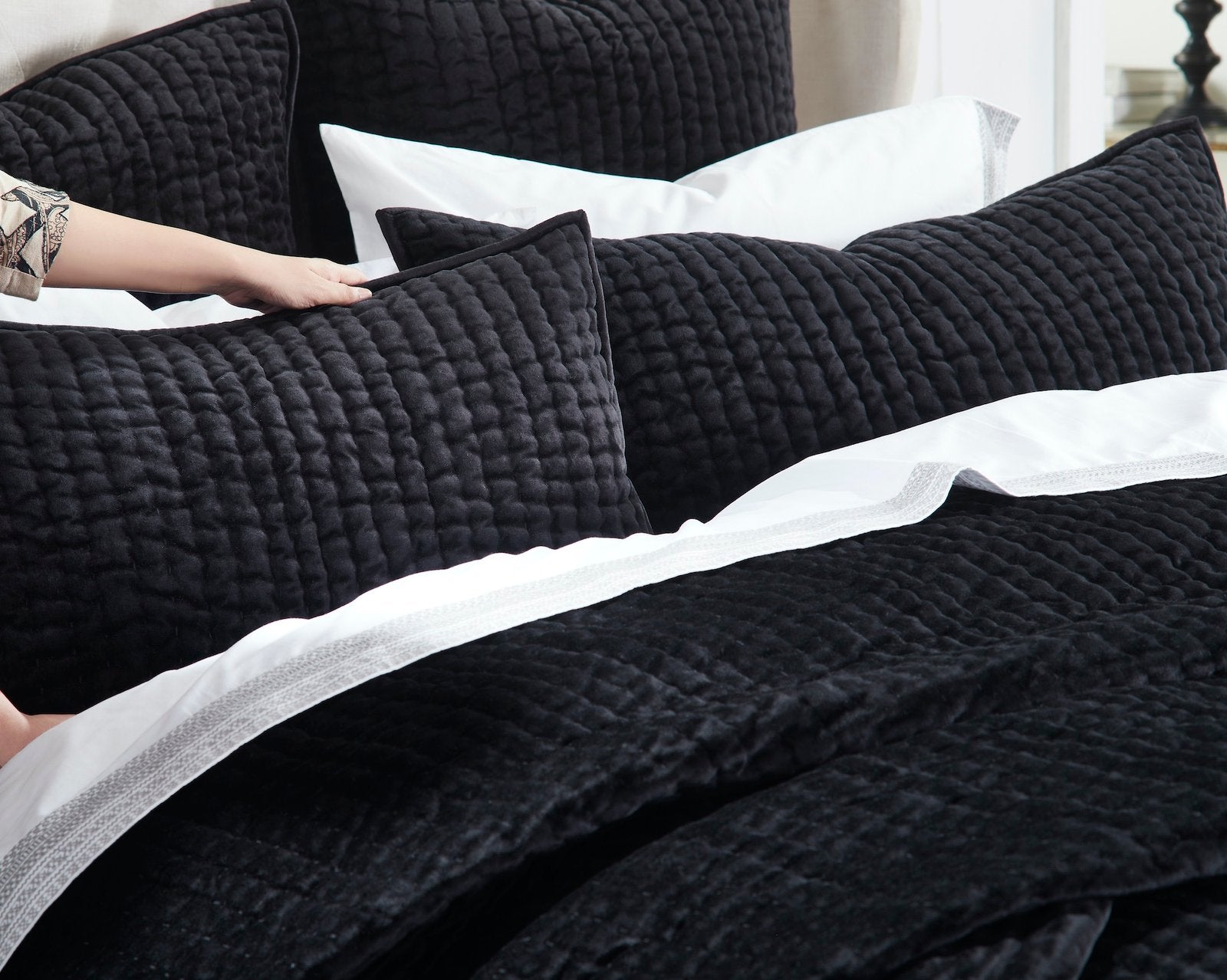 QT-361-9496_4|Hand adjusting a soft black quilted pillow, revealing the cozy textured quilt and crisp white sheets for ultimate comfort.