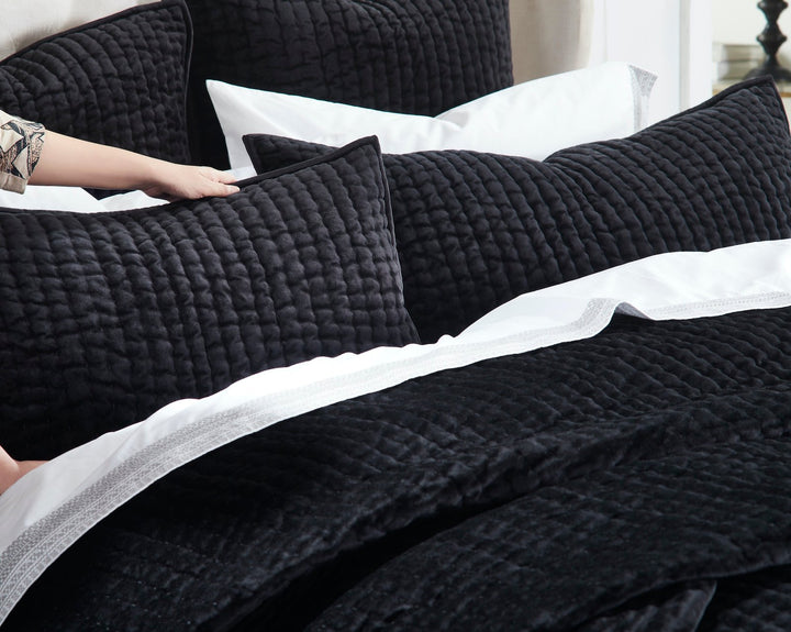 QT-361-9496_4|Hand adjusting a soft black quilted pillow, revealing the cozy textured quilt and crisp white sheets for ultimate comfort.