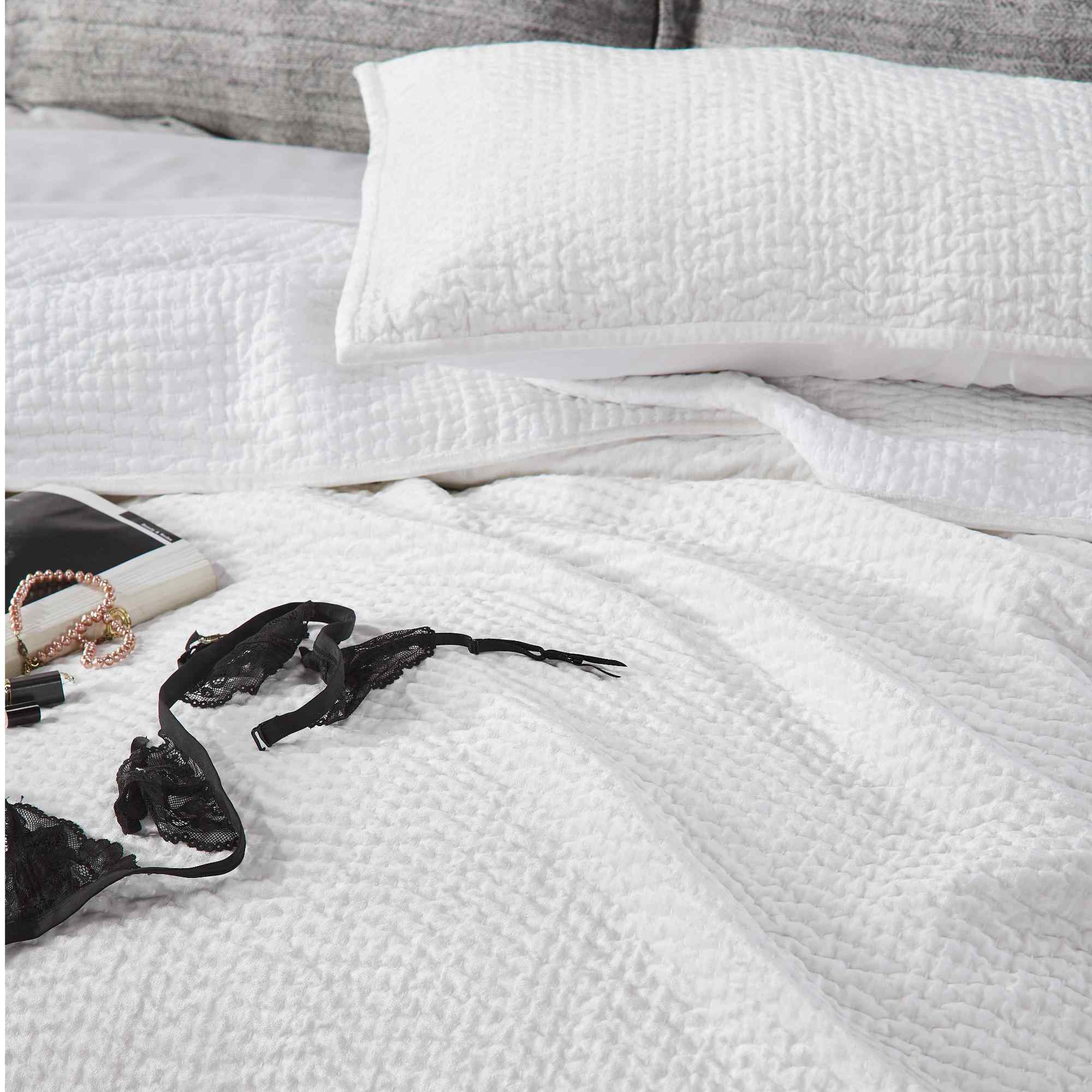 CL-182-11898_5|White textured coverlet on a bed with a black lace bra, soft quilted bedding for a cozy inviting private space. (118 chars)
