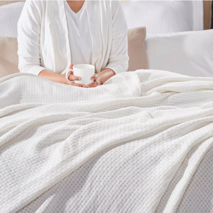 BL-852-9496_2|Person relaxing in bed with a mug, covered by a soft white waffle weave blanket, perfect for cozy morning comfort.