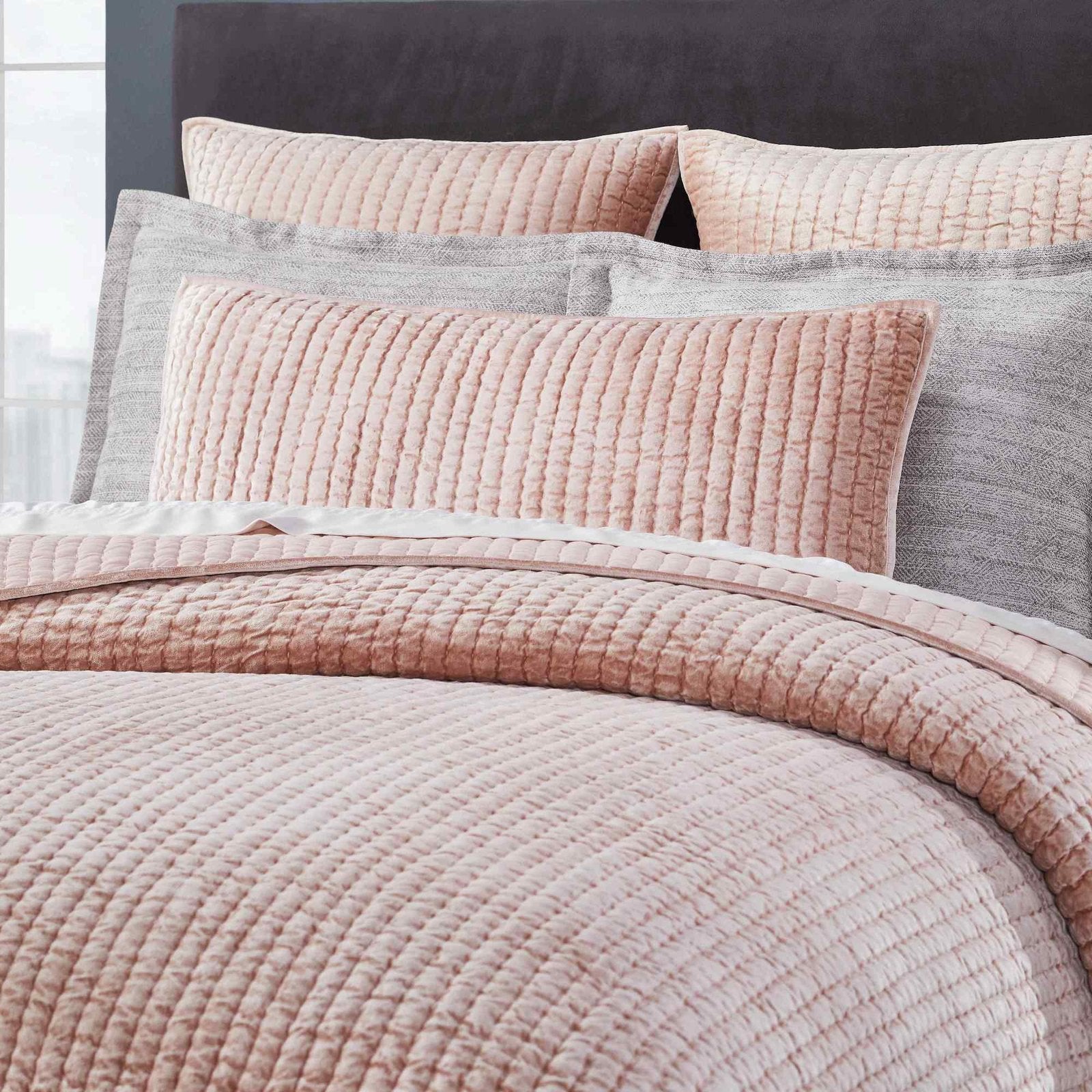 QT-354-9496_5|Close-up of dusty pink velvet channel-quilted quilt and shams on a bed. Plush texture, inviting bedroom style.
