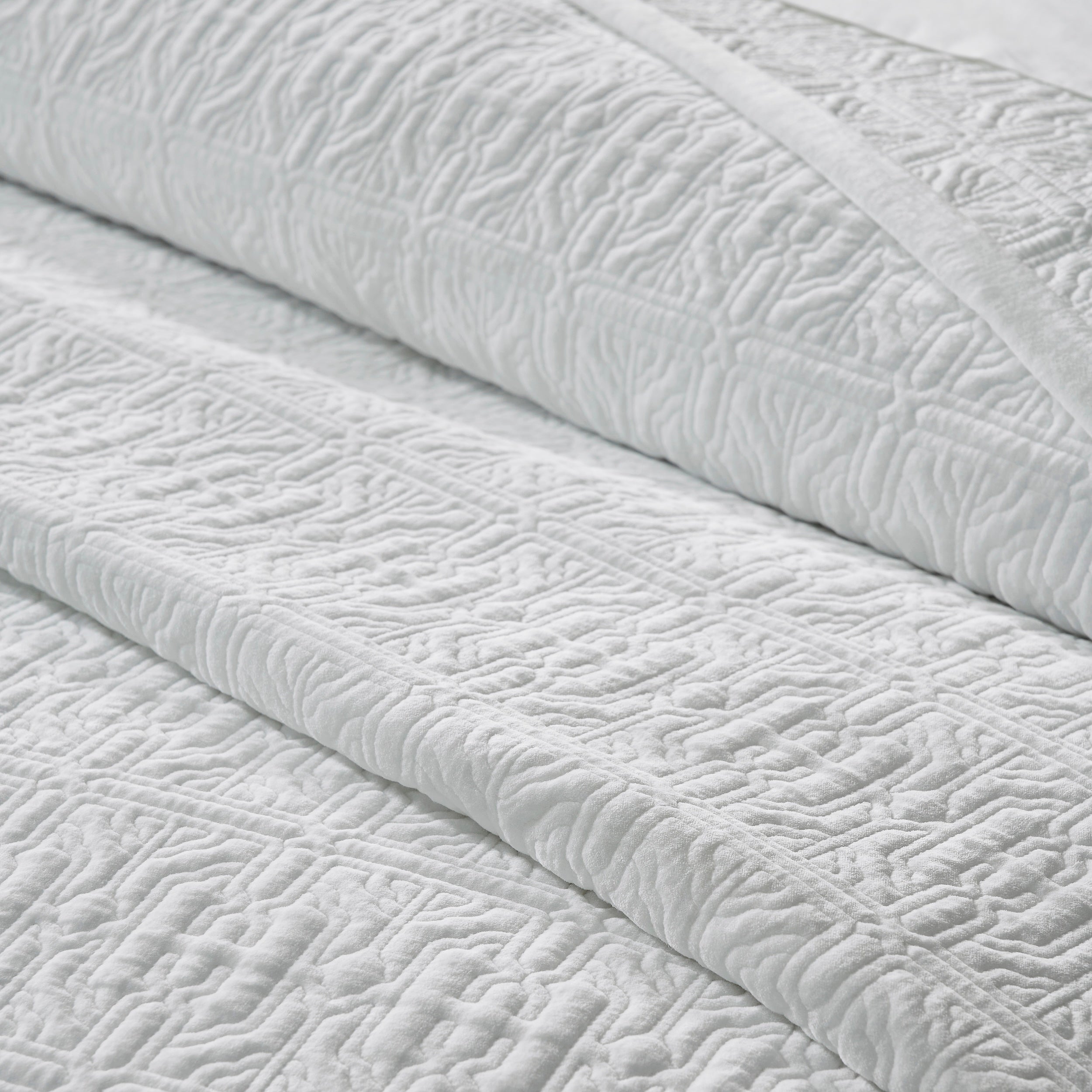 QT-376-11096_6|Close-up of a folded white patterned quilt, revealing its intricate textured design and soft material for cozy, elegant bedding.