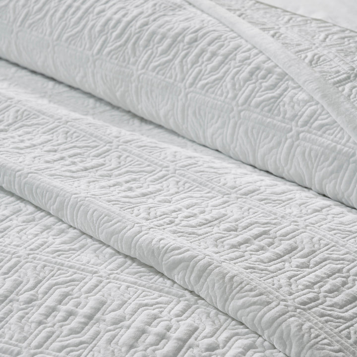 QT-376-11096_6|Close-up of a folded white patterned quilt, revealing its intricate textured design and soft material for cozy, elegant bedding.