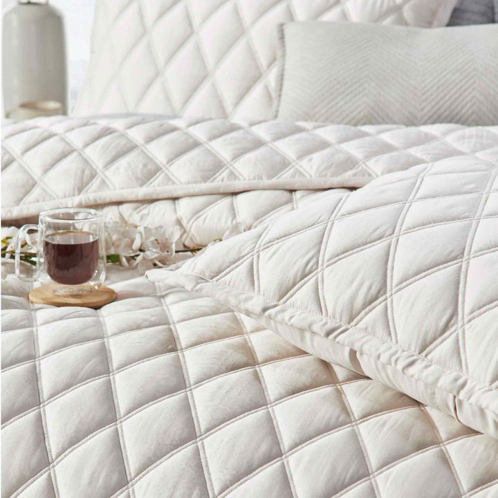 CL-180-11096_4|Cream diamond-quilted coverlet with elegant sheen, perfect for luxury bedding. Accentuated by a warm cup of tea.