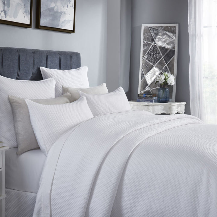 CL-200-9496_3|Close-up of a neatly arranged white quilted coverlet on a queen bed, showcasing its intricate diamond texture.
