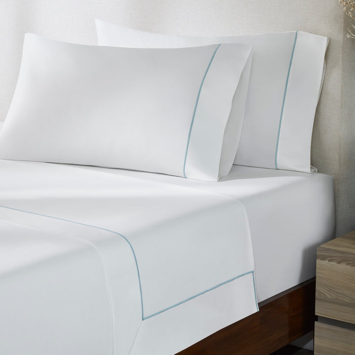 TFL-530-3980_2|Close-up of luxurious 100% cotton white sheet set with elegant light blue piping, highlighting premium bedding detail.