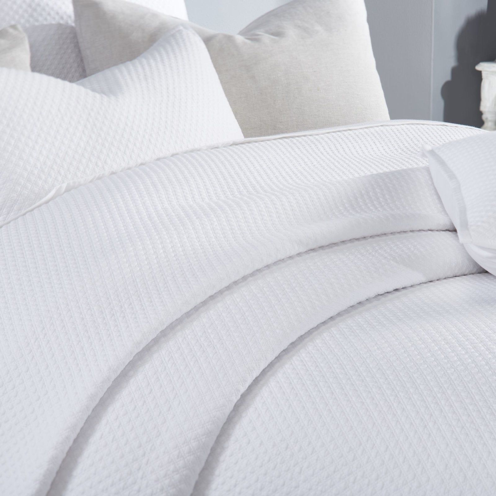 CL-200-11096_4|Soft white textured coverlet featuring a subtle diamond pattern, elegantly folded, providing cozy comfort and style.